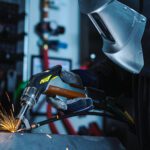 A welder in a laser welding helmet using a laser welding torch to make a long weld