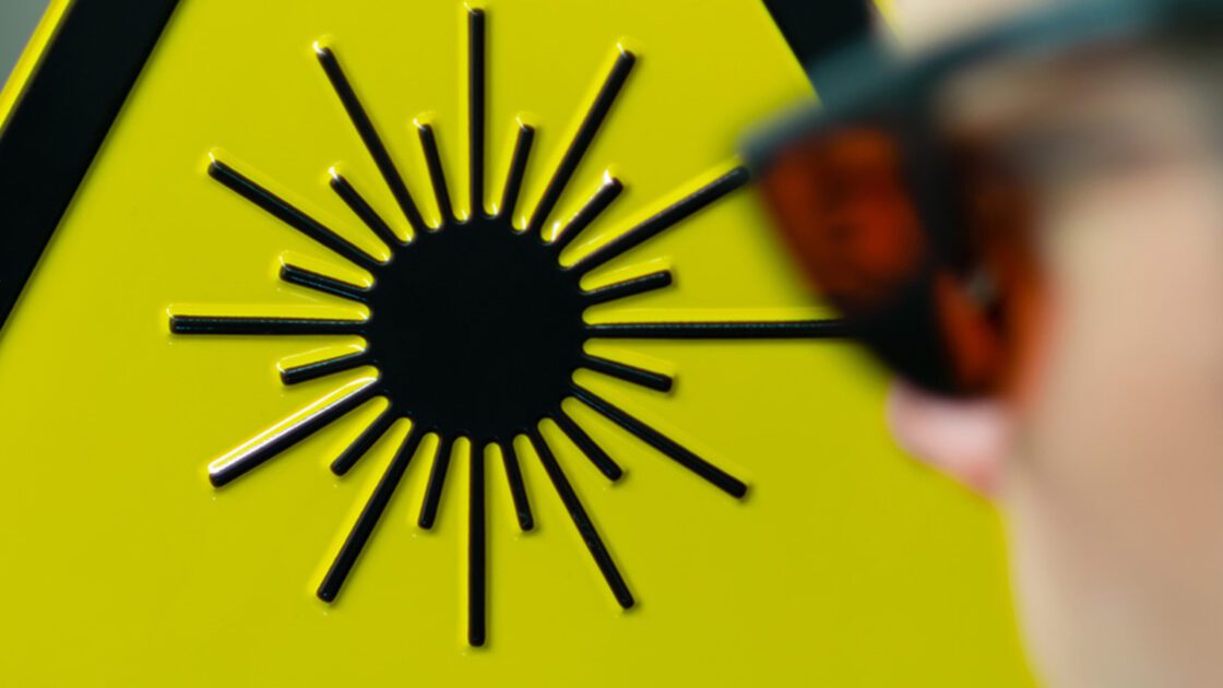 A man wearing laser safety glasses with a laser warning sign in the background